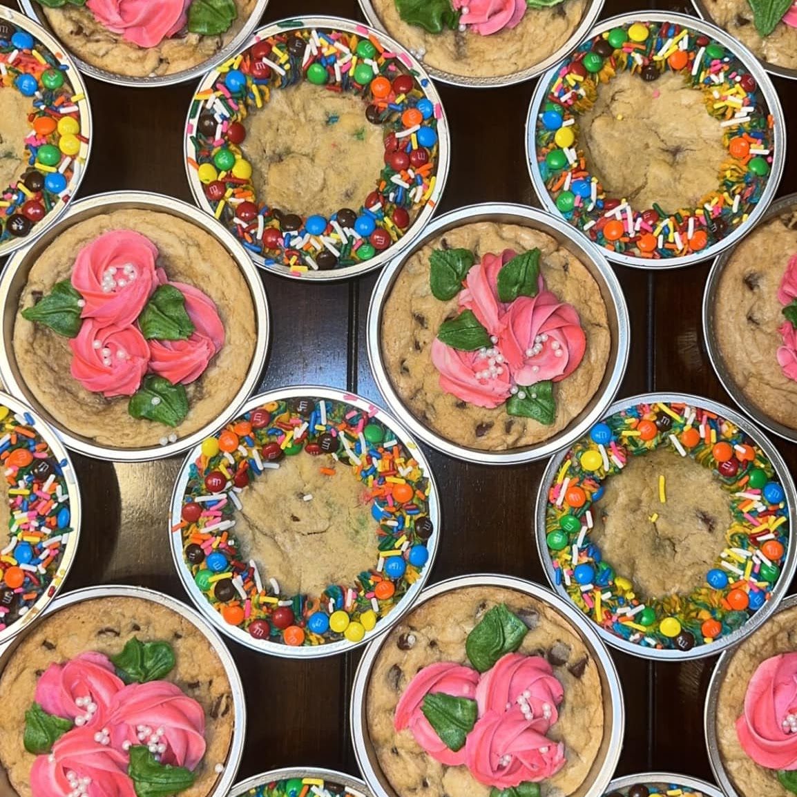 Cookie cakes topped with pink frosting roses and rainbow sprinkles