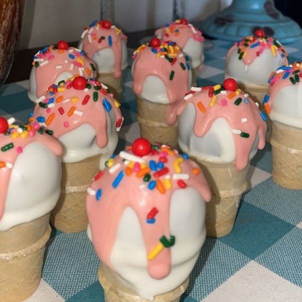 Ice cream cone cake balls dipped in pink with sprinkles and a cherry